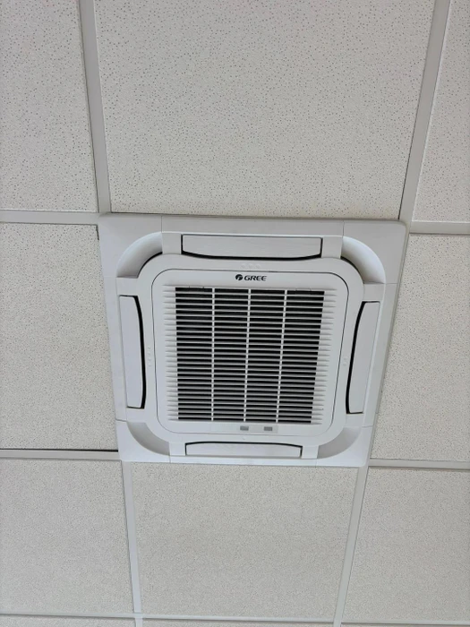Climatiseur cassette plafonnier de marque **Gree**, installé dans un faux plafond à dalles acoustiques blanches