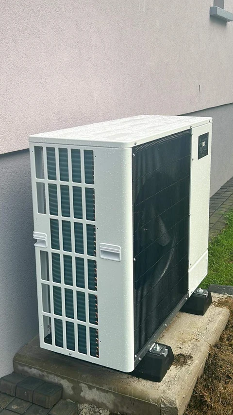 Unité extérieure de pompe à chaleur air/eau installée contre un mur de façade en crépi blanc
