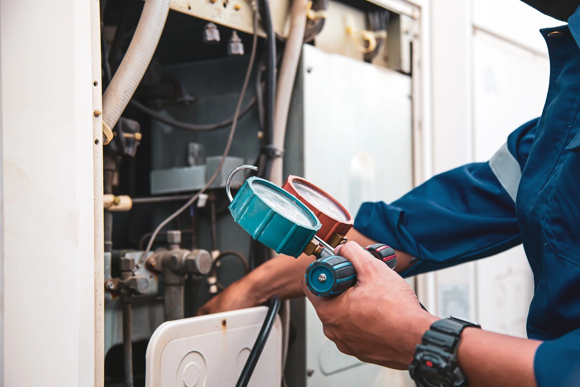 Technicien en salopette bleue et chemise à carreaux rouge effectuant la maintenance d'une chaudière à gaz domestique
