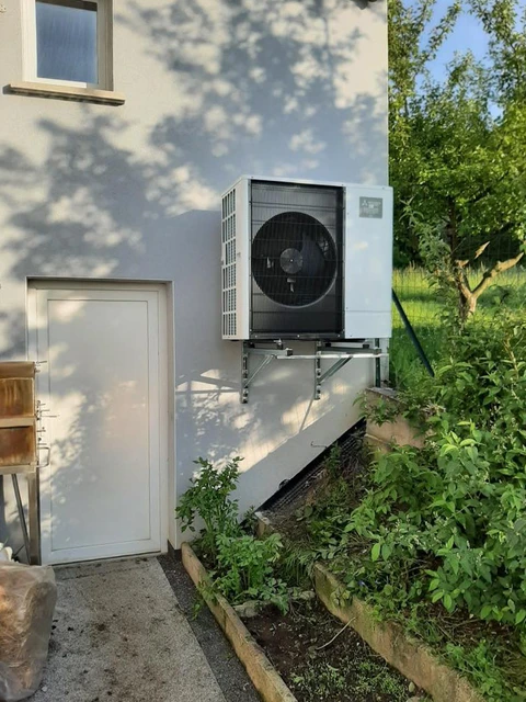 Façade extérieure d'une maison avec une pompe à chaleur air/air murale Mitsubishi Electric, modèle monobloc, montée sur un support métallique fixé au mur
