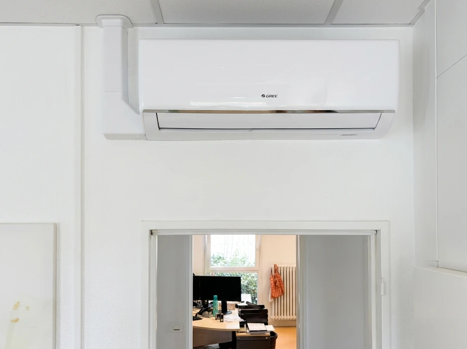 Climatiseur mural réversible **Gree** en unité intérieure, monté en hauteur sur mur blanc, au-dessus d'une porte coulissante vitrée