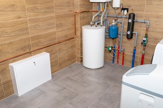 Local technique moderne avec chauffe-eau électrique cylindrique blanc, vase d'expansion bleu, collecteur de distribution avec vannes colorées rouge et bleue, tuyauterie cuivre et PER