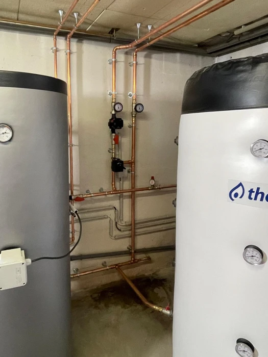 Sous-sol technique avec deux ballons de stockage d'eau chaude sanitaire raccordés par un réseau de tuyauterie en cuivre